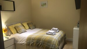 A neatly made bed with a plaid blanket and pillows, a bedside table with a lamp and a vase of sunflowers, and a small cabinet to the right. - Private Room - Sleeps 2 - Private Entry - Parking (Solihull)
