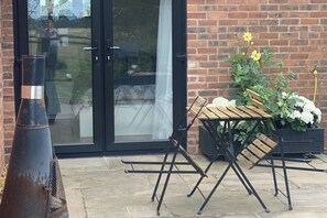 An outdoor seating area with a brick wall, a glass door, and a metal planter with flowers. - Private Room - Sleeps 2 - Private Entry - Parking (Solihull)