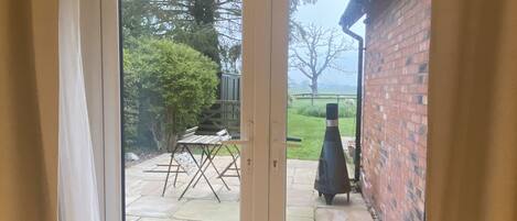 A patio area with a table and chairs, a brick wall, and a grassy lawn visible through a glass door.