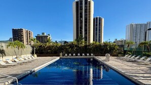 A swimming pool with lounge chairs and a stone deck, surrounded by tall buildings. - Renovated - Diamond Head and Ocean Views! - FREE Parking - 1 Block to Beach (Honolulu)