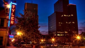 A nighttime cityscape with illuminated buildings and streetlights. - Dreaming Rose City Getaway! (Tyler)