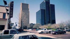 A city street with modern buildings, parked cars, and a visible 'TYLER' sign. - Dreaming Rose City Getaway! (Tyler)