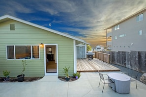 A residential backyard with a wooden deck, a patio table, and potted plants.