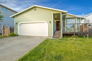 A single-story house with a white garage door, a front porch with a wooden railing, and a small set of stairs leading to the entrance.