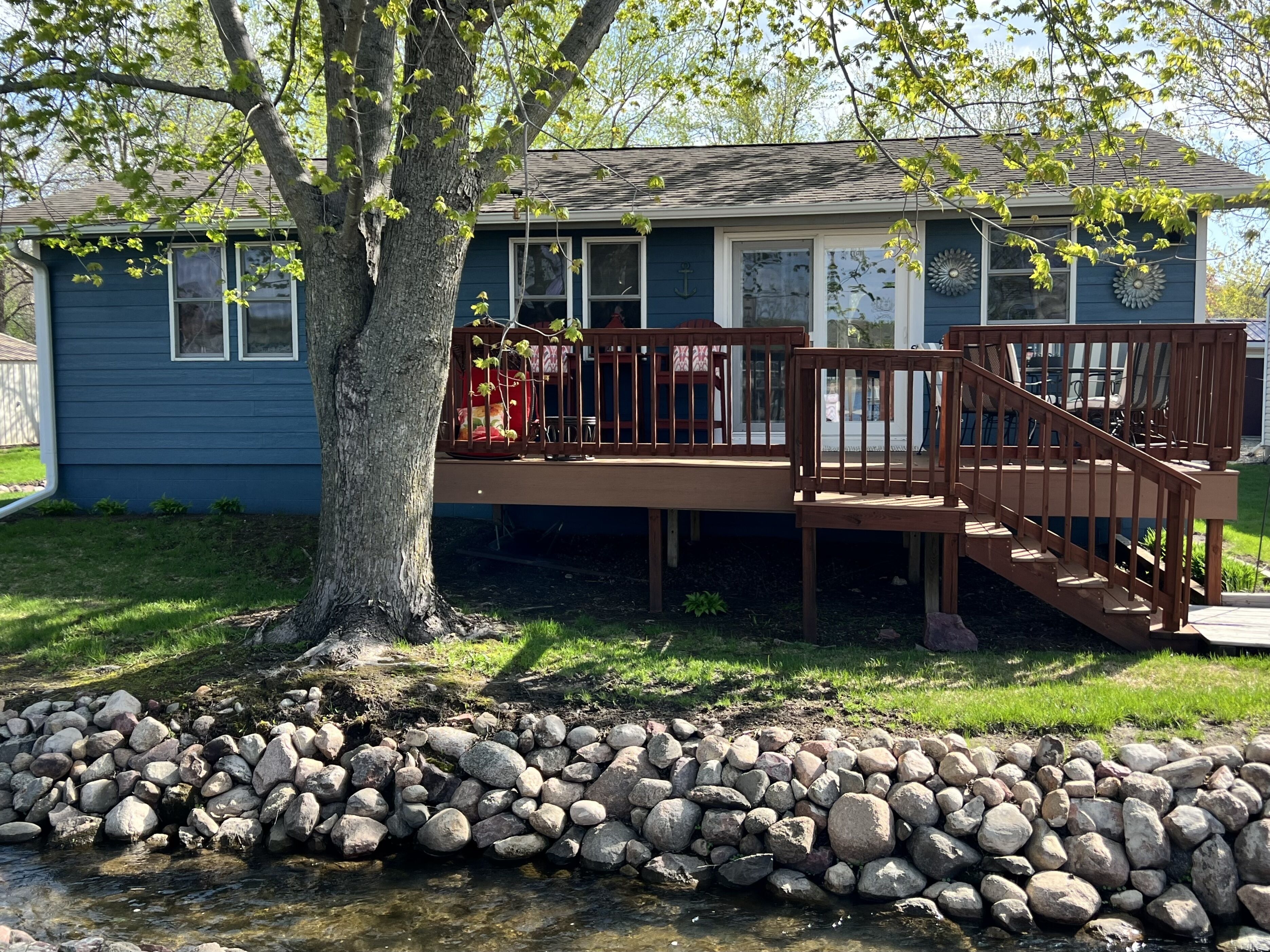 A residential deck with a wooden railing, a small staircase, and a stone wall in front.