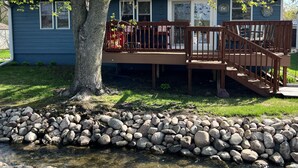 A residential deck with a wooden railing, a small staircase, and a stone wall in front. - Lakeview Cabin (Spirit Lake)