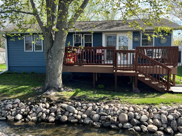 A residential deck with a wooden railing, a small staircase, and a stone wall in front.
