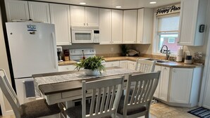 A kitchen with white cabinets, a microwave, a stove, and a refrigerator. There is a dining table with chairs and a potted plant on it. - Lakeview Cabin (Spirit Lake)