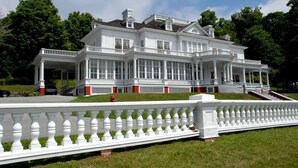 A large, white, two-story house with a symmetrical facade, multiple windows, and a covered porch.