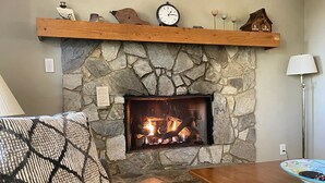A stone fireplace with a fire, a wooden shelf above it, and a lamp to the right.