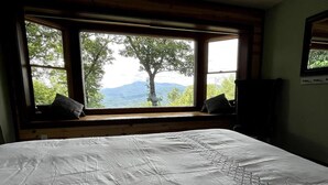 A bedroom with a large bed, a window with a view of trees and mountains, and a wooden headboard.