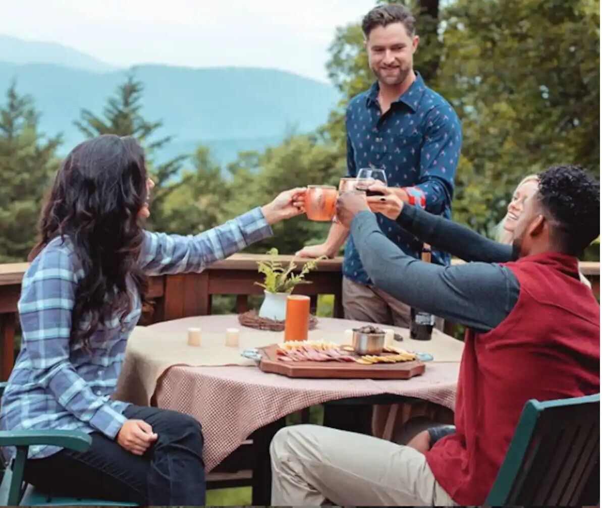 Eine Gruppe von Menschen sitzt an einem Tisch im Freien und genießt eine Mahlzeit, umgeben von einer natürlichen Landschaft.