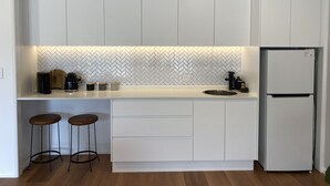 A compact kitchen with white cabinets, a herringbone tile backsplash, a built-in sink, and a refrigerator.