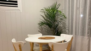 A dining area with a round table and four chairs, a potted plant, and a window with blinds.