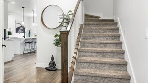 Eine Treppe mit Holengeländern und Steinernen Stufen führt zu einer Küche mit weißen Schränken und einem Esstisch.