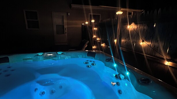 Ein Whirlpool mit blauem Licht, umgeben von einem Holzzaun und einem Haus im Hintergrund.