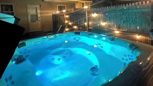 Ein Whirlpool mit Holzterrasse und Umzäunung, umgeben von einem Haus und Bäumen.