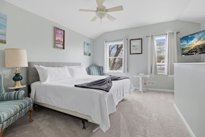 A bedroom with a bed, a chair, a nightstand, a TV, and a ceiling fan.