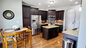 A modern kitchen with dark wood cabinets, stainless steel appliances, and a wooden dining table. - 🌟"Home-Away-From-Home" Beauty; Kid, Baby & Dog-Friendly; Veteran-Owned🌟 (Sanford)