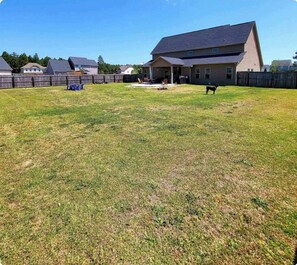 A residential backyard with a house, a wooden fence, and a dog. - 🌟"Home-Away-From-Home" Beauty; Kid, Baby & Dog-Friendly; Veteran-Owned🌟 (Sanford)
