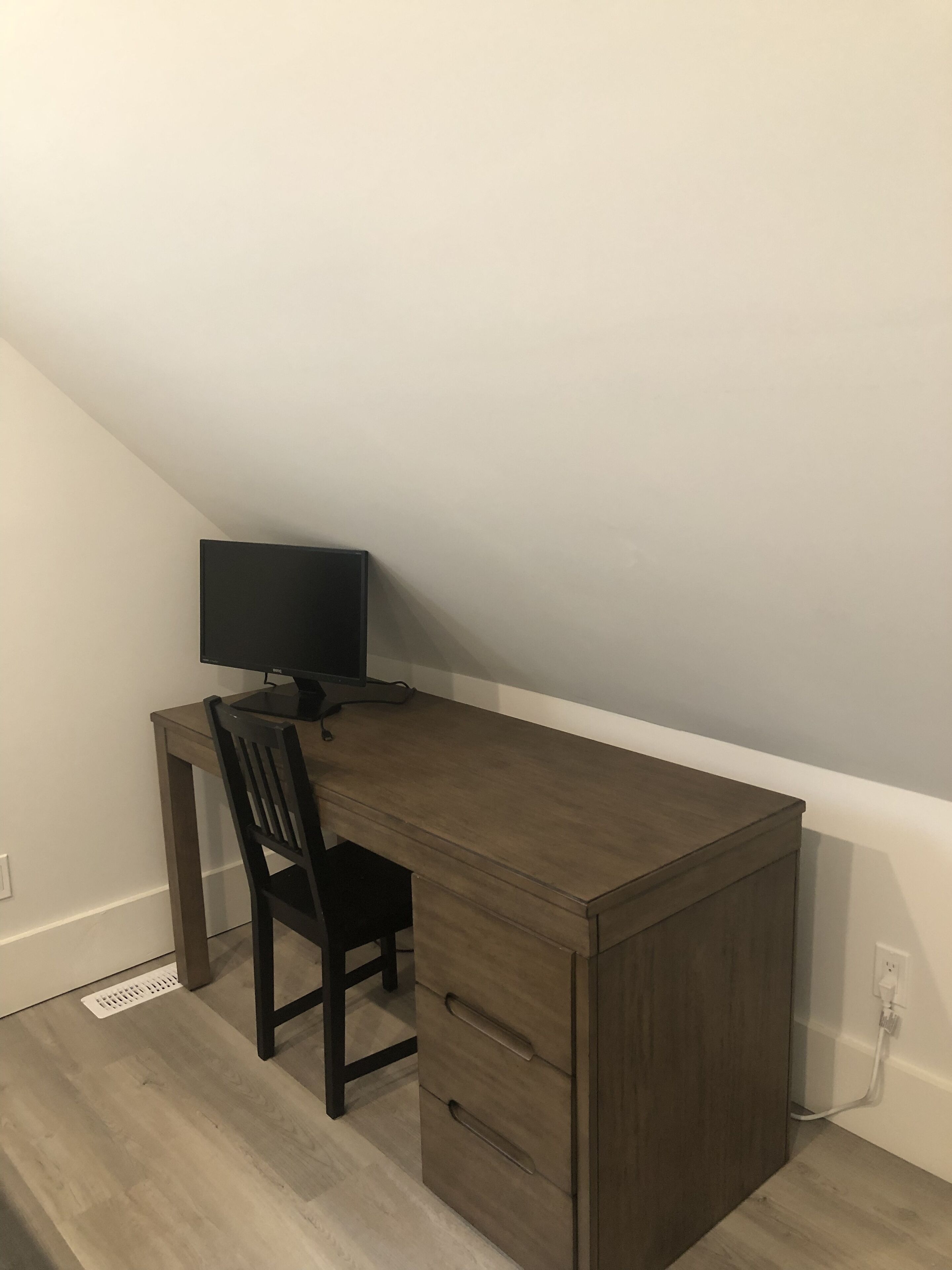 A corner desk with a chair, a flat-screen monitor, and a drawer unit.