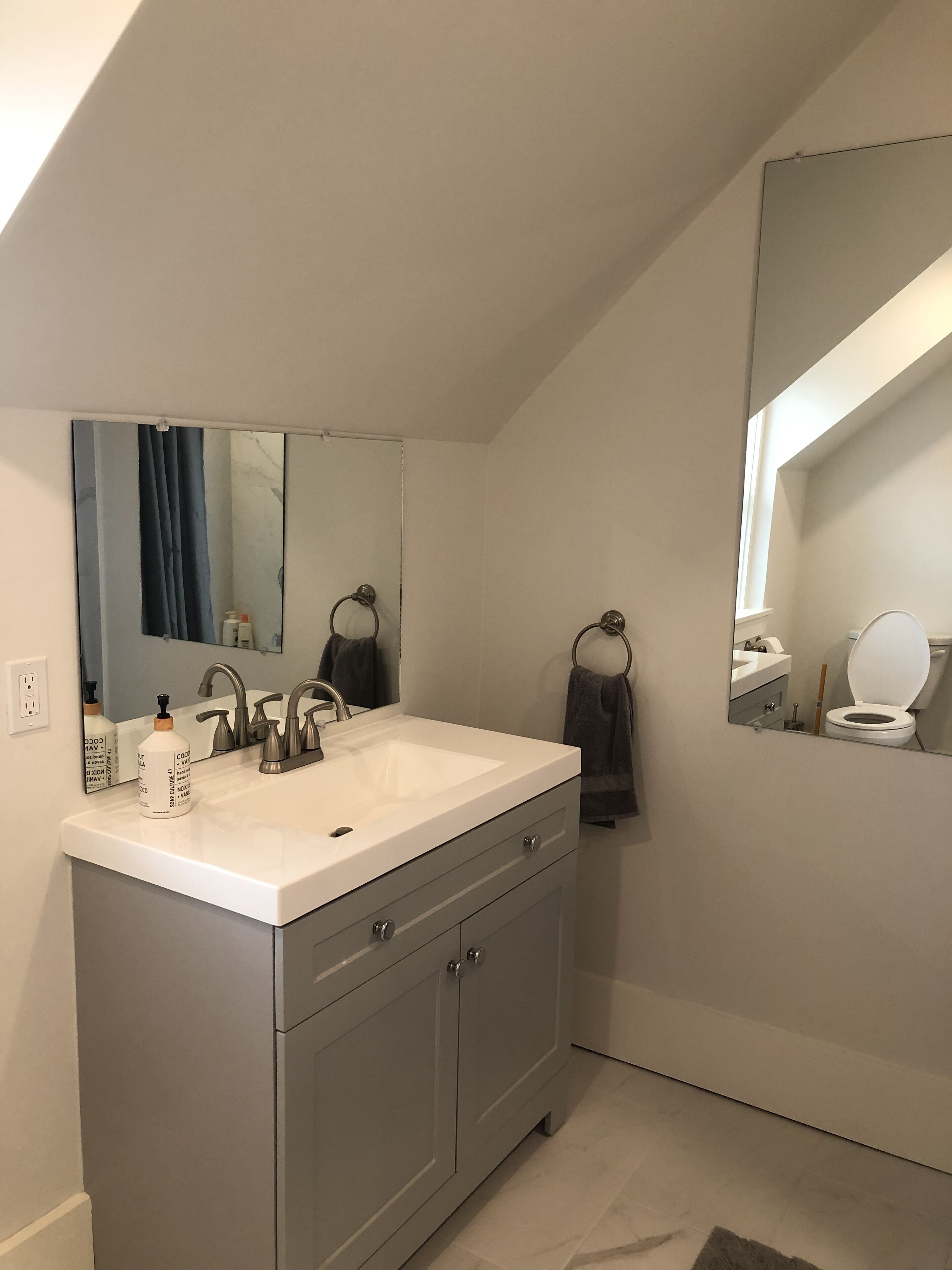 Un baño moderno con tocador blanco, un espejo grande y un inodoro.