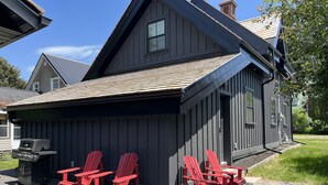 Une cabane en bois sombre, dotée d’un toit en pente, d’un petit porche avec des fauteuils Adirondack rouges et d’un barbecue à l’extérieur.