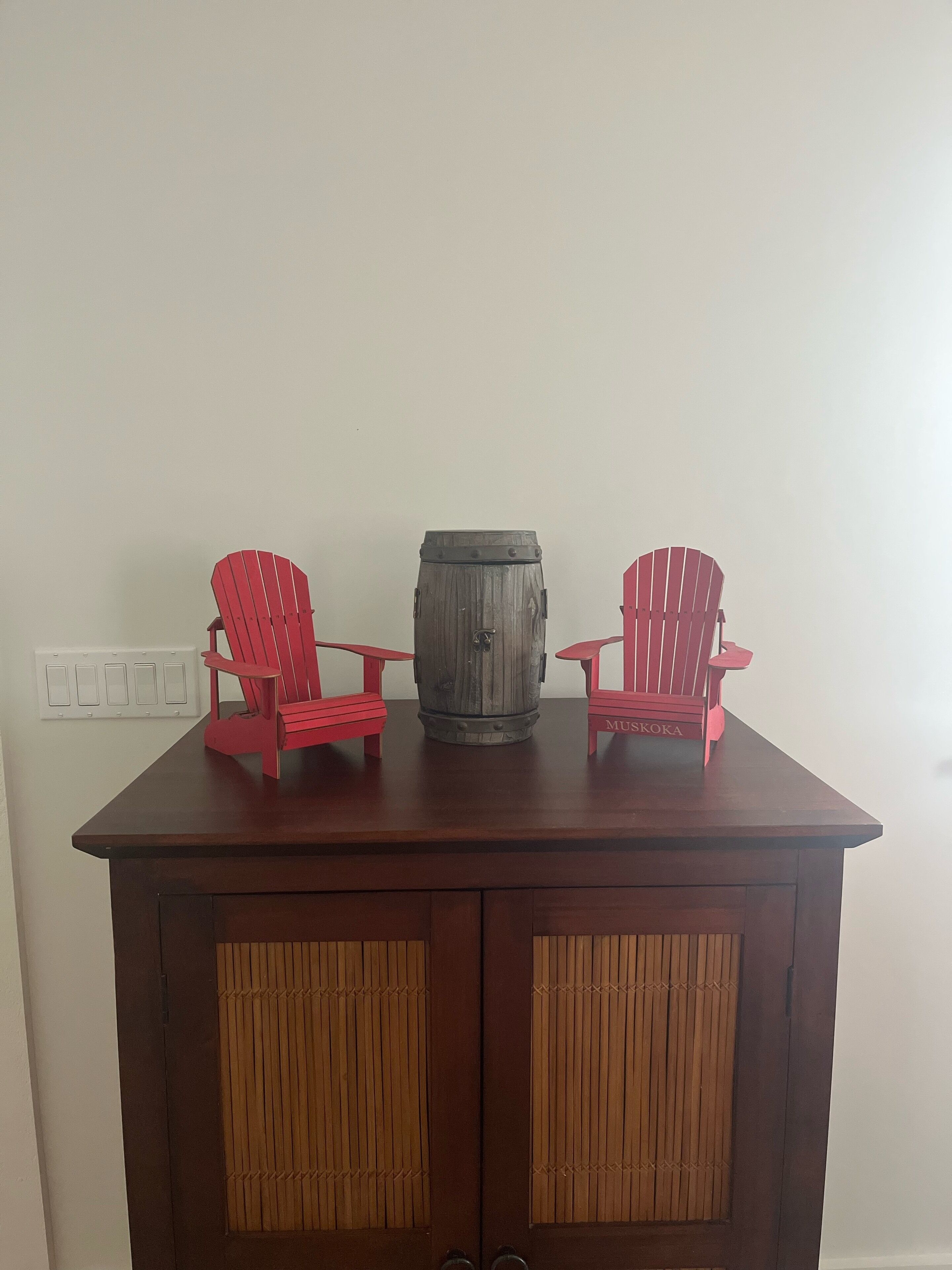 A wooden cabinet with two red Adirondack chairs and a wooden barrel on top.