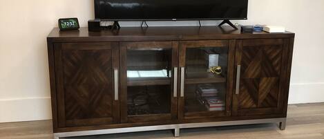 A living room with a TV on a wooden cabinet, a coffee table with remote controls and magazines, and a tissue box.