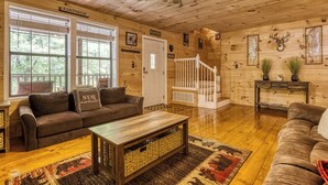 A cozy log cabin interior with a wooden ceiling, a staircase, a brown leather sofa, a coffee table, and a fireplace. - Cozy Cabin Hot tub Firepit Game Room Pool Table Gas Fireplace 5 min to GB-PF (Sevierville)