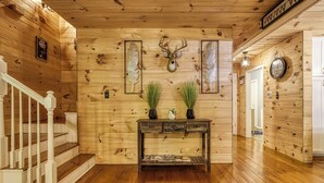A wooden interior with a staircase, a console table with decorative items, and a deer head mounted on the wall. - Cozy Cabin Hot tub Firepit Game Room Pool Table Gas Fireplace 5 min to GB-PF (Sevierville)