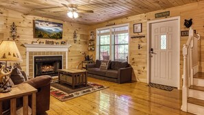 A cozy log cabin interior with a fireplace, wooden furniture, and a staircase. - Cozy Cabin Hot tub Firepit Game Room Pool Table Gas Fireplace 5 min to GB-PF (Sevierville)