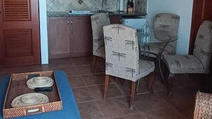 A spacious living room with a blue ottoman, a dining area with chairs, a ceiling fan, and a kitchen area with cabinets and a microwave.
