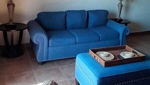 A living room with a blue sofa, a small table, and a wicker chair. - Suit Rivas 132 Gran Pacifica Resort (Villa El Carmen)
