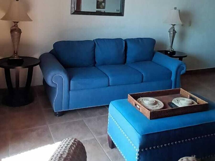 Uma sala de estar com um sofá azul, uma mesinha e uma cadeira de vime.