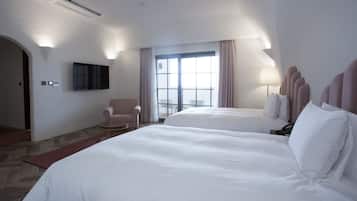 A hotel room with two beds, a TV mounted on the wall, a chair, and a balcony with a view.