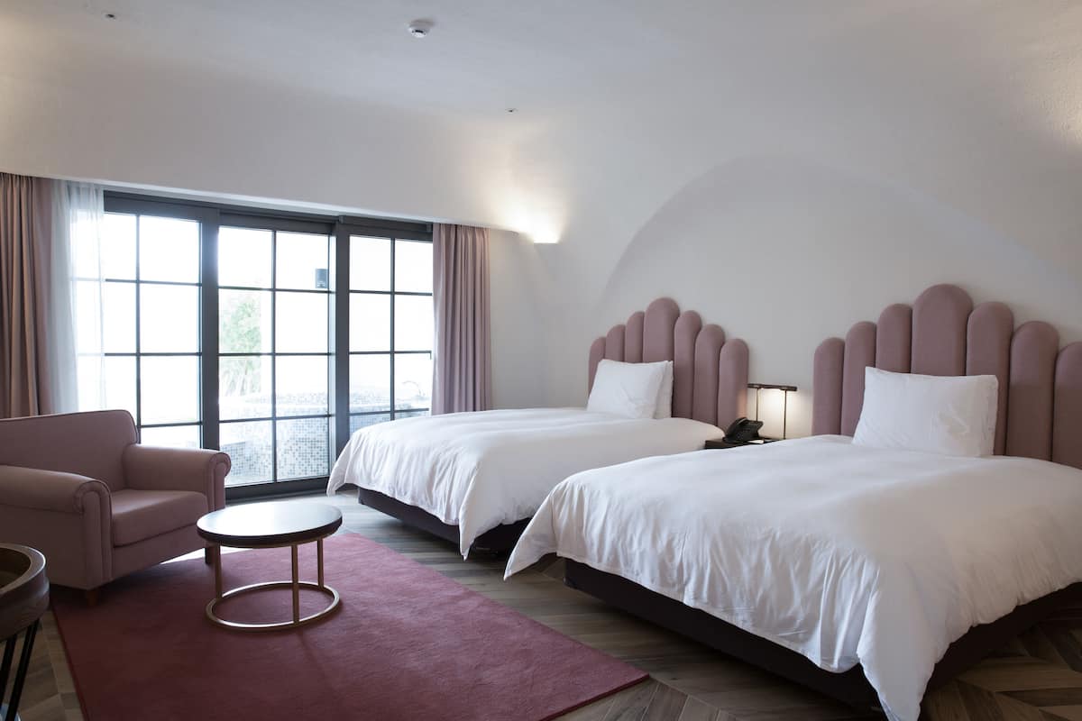 A hotel room with two beds, a sofa, a small table, and a large window with curtains.