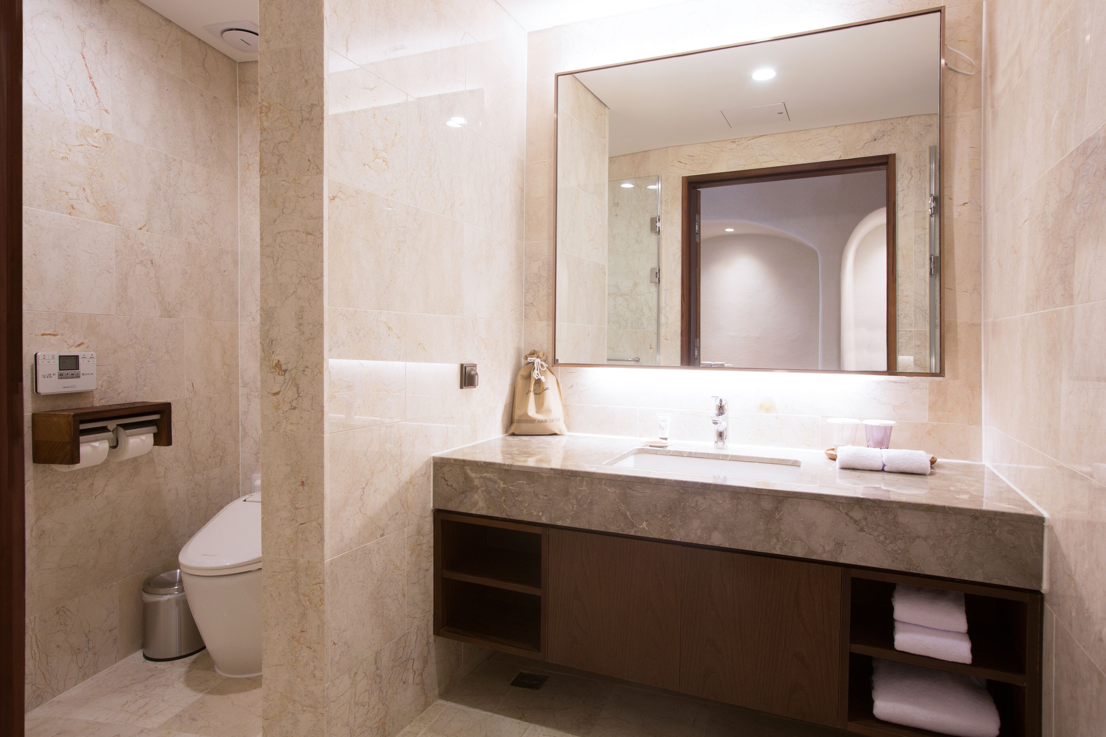 A modern bathroom with a marble sink, a large mirror, and a toilet.