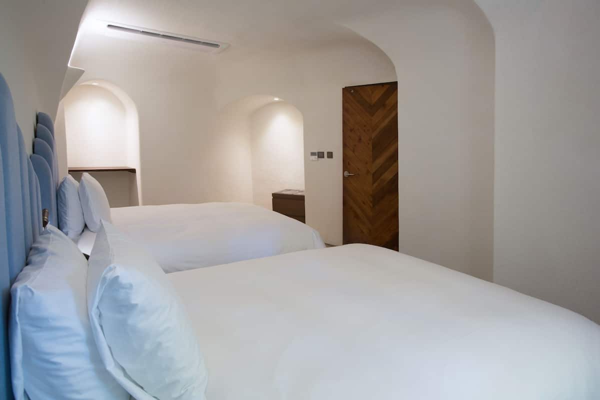 A hotel room with two beds, a wooden door, and a small bedside table.