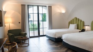 Hotelkamer met twee bedden, een slaapbank, een tafeltje en een groot raam met gordijnen.