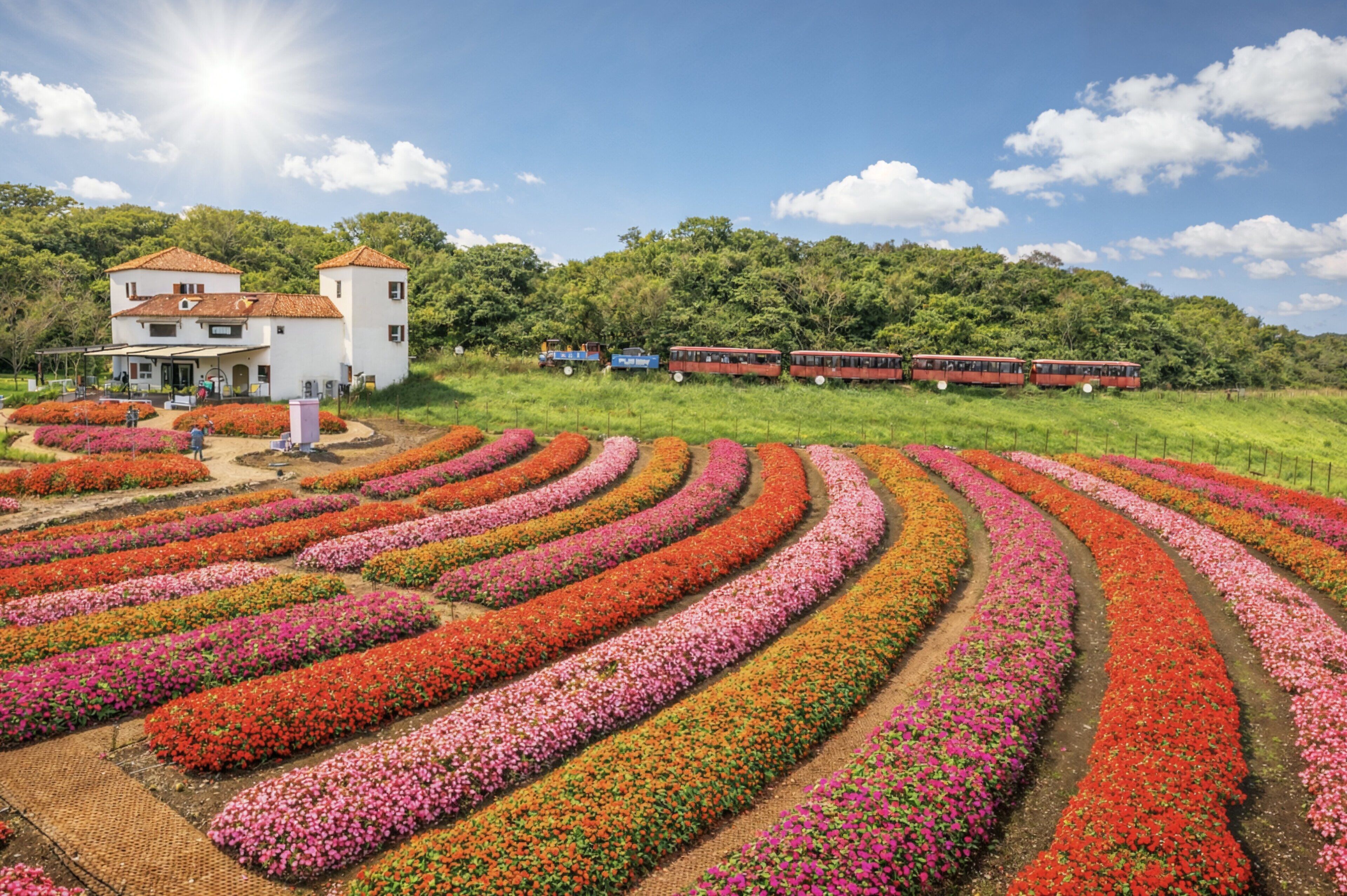 A white building with a red roof, surrounded by a garden with rows of colorful flowers.