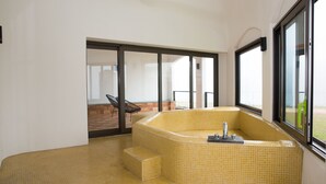 Een moderne badkamer met een ruime badkuip, een klein zitgedeelte en uitzicht door grote ramen.