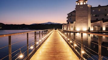 A wooden bridge with lights, leading to a building with a tower, by a body of water.