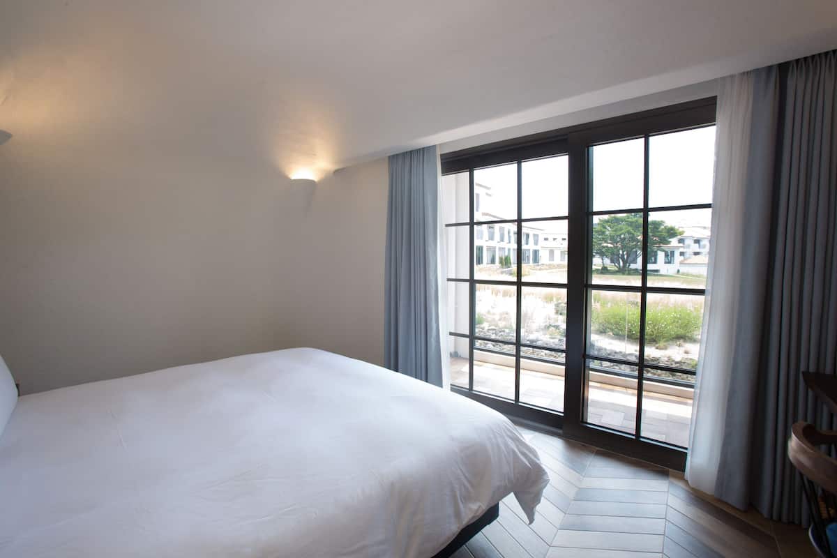 A hotel room with a large bed, a window with curtains, and a view of buildings outside.