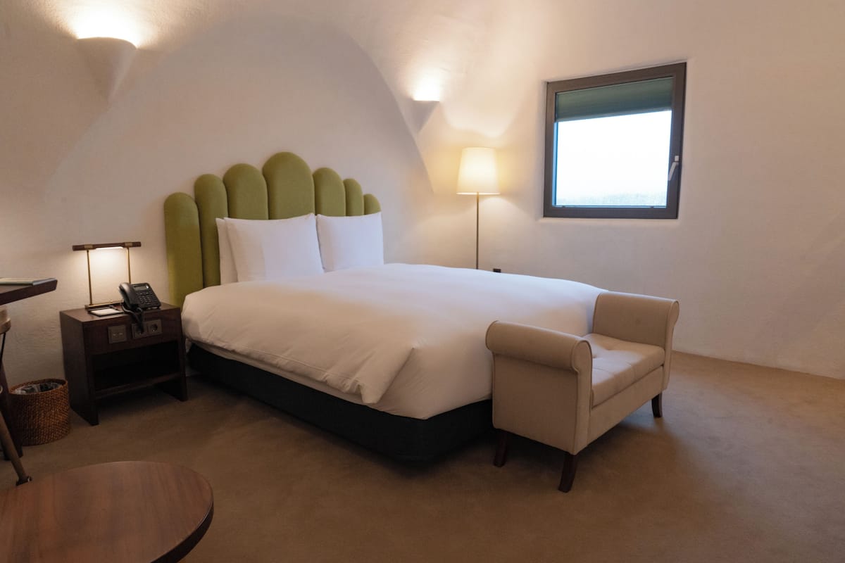 A bedroom with a bed, bedside table, lamp, chair, and a window.