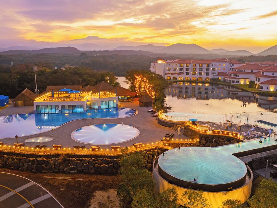 A resort with multiple swimming pools, a large central pool, and a view of surrounding hills.