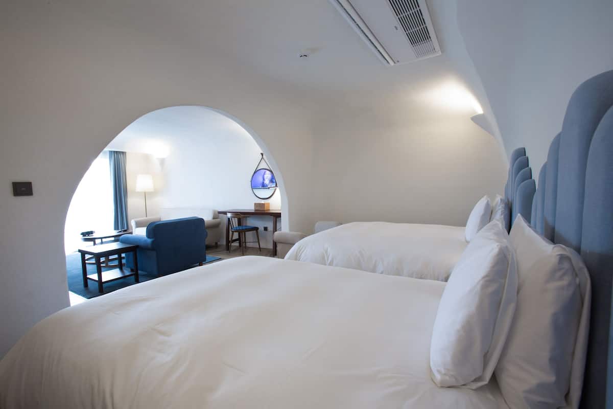 A hotel room with two beds, a desk, and a chair.