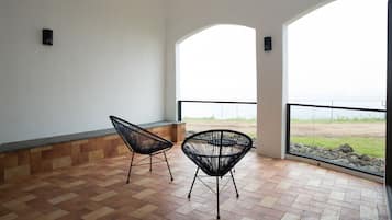 Un balcon avec deux chaises noires, un sol carrelé et une vue sur la plage, visible à travers de grandes fenêtres.