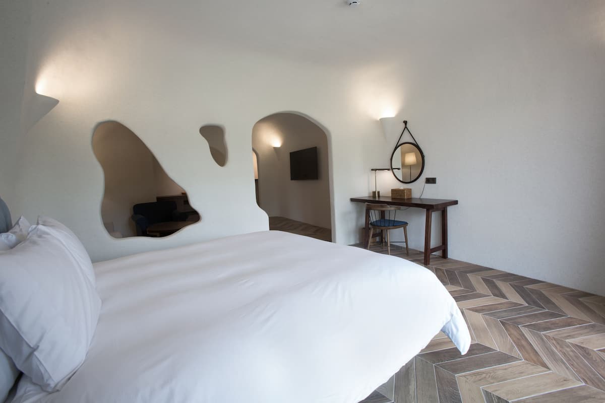 A hotel room with a large bed, a desk with a chair, and a mirror.