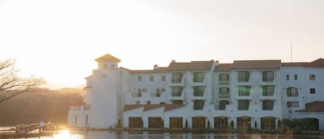 Un edificio blanco grande con varios balcones y una torre, ubicado junto al agua.